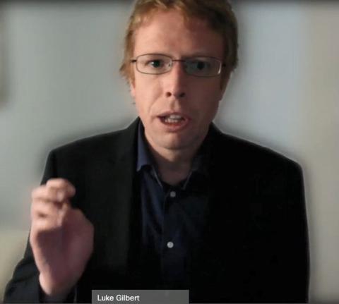 Gilbert with fingers pinched talks via videocast. 