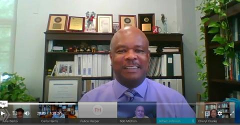 A smiling Dr. Johnson at his desk asks Harris an audience member's question via videocast.