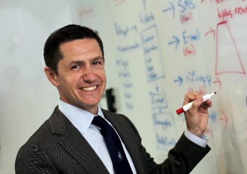Dr. Ryan Shaw stands holding a marker, about to write on a whiteboard.