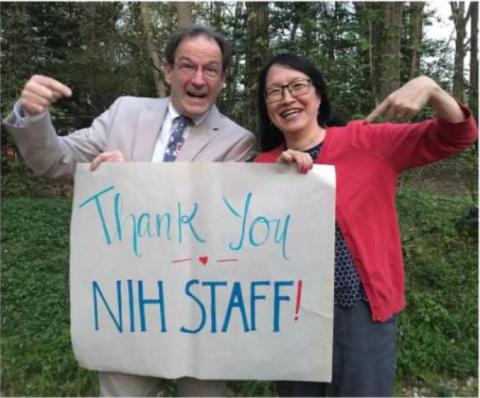 Holland and Pao, both smiling, hold up a poster board sign that says, "Thank you NIH staff!"