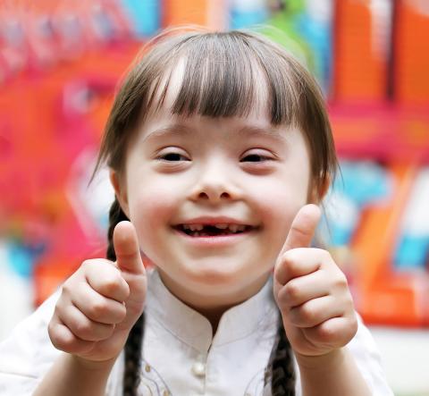 Little girl with Down syndrome smiles and gestures thumbs up