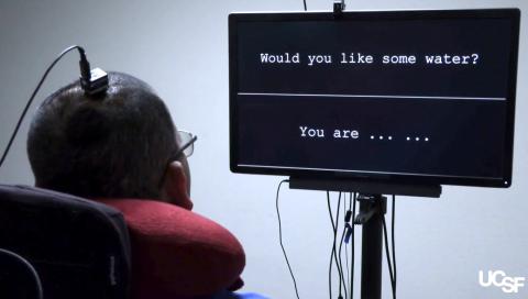 Person with an electrode attached to head faces a computer screen showing a full sentence and words of another sentence.
