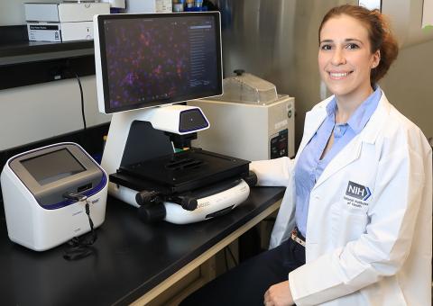 Sadtler sits in lab in front of a computer screen and microscope.