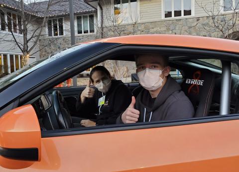 Jen and Luke give thumbs up sitting in Driven to Cure car in front of the Children's Inn.