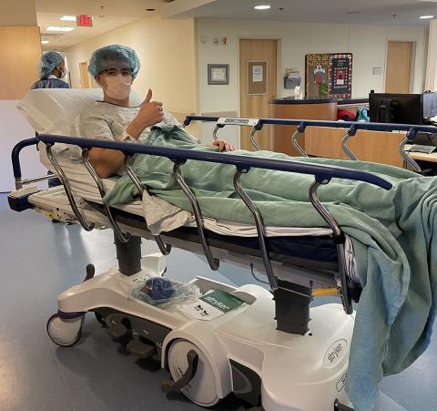 Luke gives thumbs up on hospital bed in hallway of the Clinical Center.