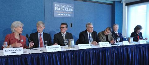 Seated at a long conference table draped in blue at the National Press Club, Collins and Sebelius chat as pharmaceutical leaders look on.