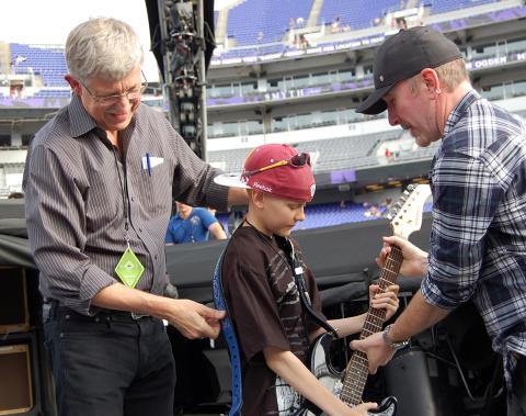 Collins stands on stage at Capital One Arena fixing the guitar strap on a young patient as the Edge hands the child his guitar.