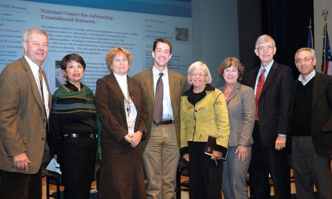 Collins stands with the first NCATS leadership team on stage with a slide of the NCATS website behind them.