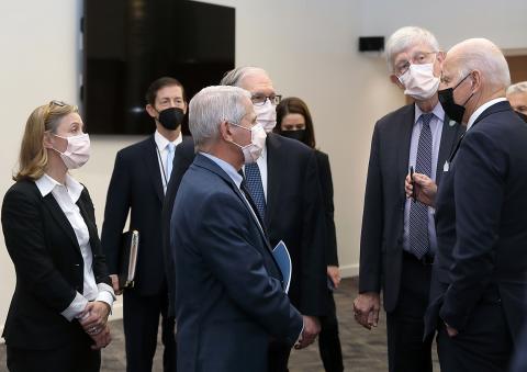 Several people in masks stand chatting informally with President Biden.