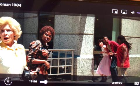 Flood, in red jacket, with other background actors in a scene on the streets of DC