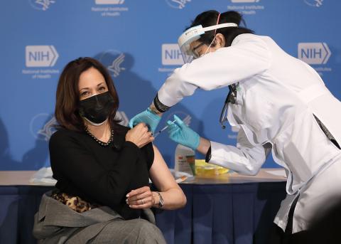 Seated with left arm exposed, Harris receives her shot from Judy Chan.
