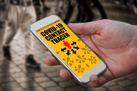 A hand holds a smartphone with bright yellow screen showing covid contact tracing app, in a crowd of people