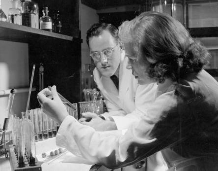 A researcher holds a vial of insulin as another researcher looks on, surrounded by vials in the lab.
