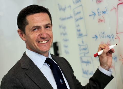A smiling Shaw stands holding a marker up to a dry-erase board.
