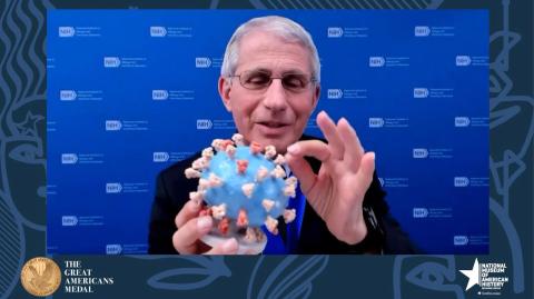 Dr. Fauci, holding a 3-dimensional model of the SARS-CoV-2 virus, pinches one of the orange spikes.