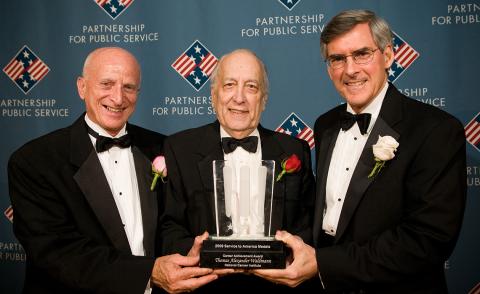 Waldmann in formal attire holding statuette, flanked by 2 other gentleman in formal attire