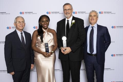 Four individuals, two with trophies in hand, stand smiling for camera