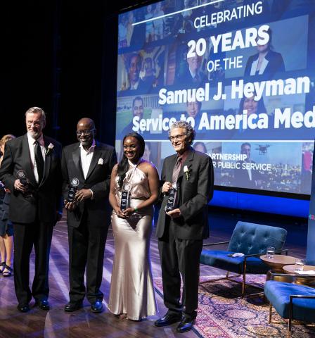 Four individuals in formal dress holding trophies smile with Sammies backdrop behind them.