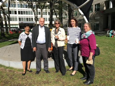 Five individuals smile outside in front of an office building