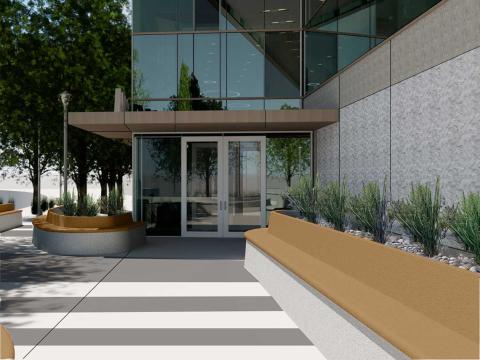 A crosswalk with a long wooden bench lead up to the modern, glass building.