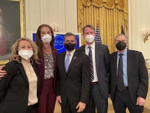 group photo of five individuals in face masks with the East Room of the White House behind them.