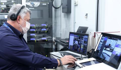 Burnham sits in office with 2 laptops on desk and computer servers and other equipment behind him.