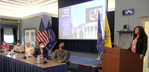 White speaks from podium, as panelists observe