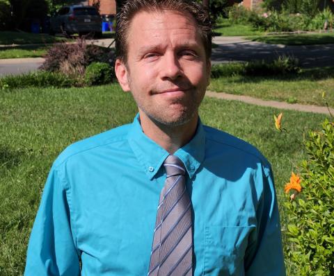 Kosub in blue shirt and grey tie standing on grass on NIH campus