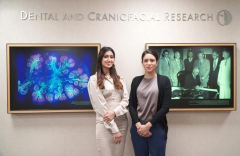 Singh and Leinbach stand in front of NIDCR wall with framed research image and historic photo behind them.