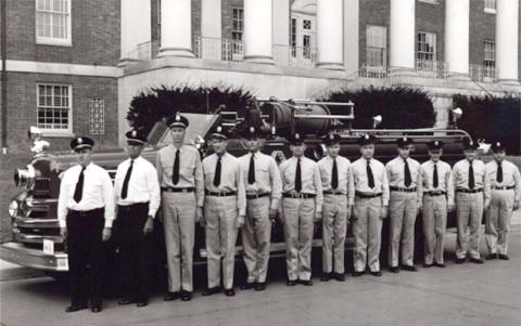 Black &amp; white photo of fire department staff standing next to fire truck in front of Bldg. 1