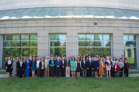 A large group of people pose for a picture outside of a gray building with large windows. 