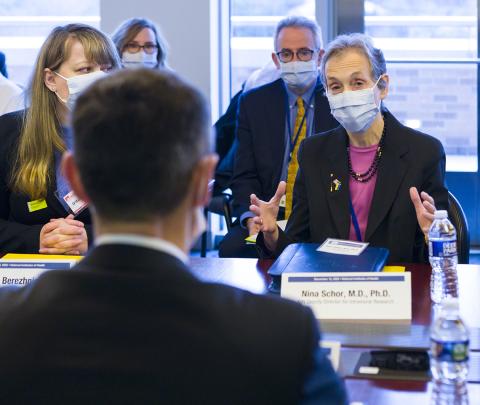 Schor seated with hands cupped in front of her address the minister. 