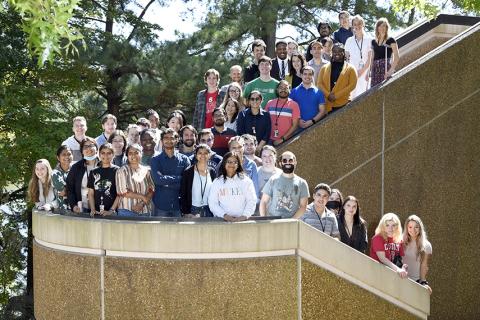 Large group of fellows stand together outside, winding around a staircase