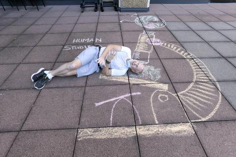 A man lies on ground beside microscope drawn in colorful chalk and the words "human studies"