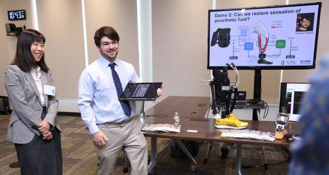 Two doctors stand describing their work, with computer monitor showing graphics with the headline: Demo 1: can we restore sensation of prosthetic foot?