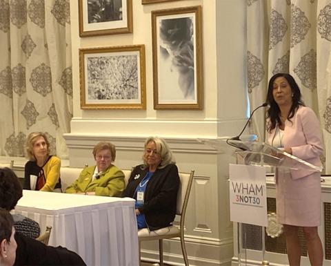Clayton speaks at podium as two former congresswomen and Dr. Pinn look on in a reception room