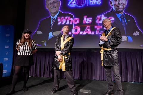 A referee stands next to Green and Collins, each wearing silk black robes with yellow sashes over ther suits.
