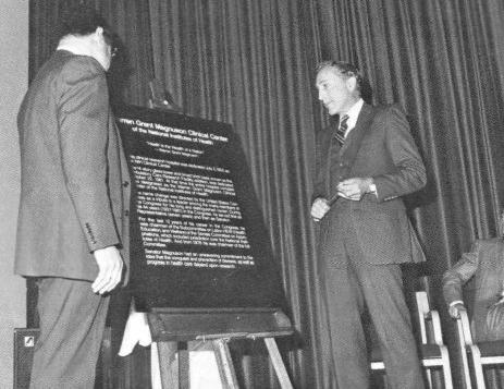 Two men stand in between a plague in Masur Auditorium