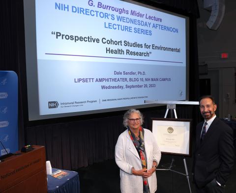 Sandler and Zeldin stand by lecture poster on Lipsett stage.