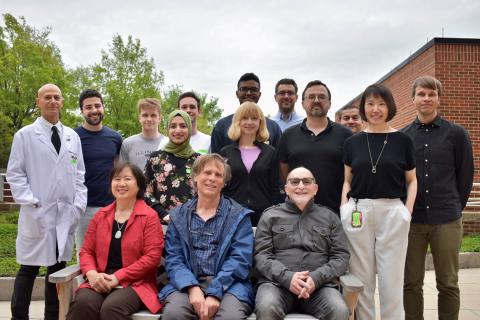 Members of the Lipoprotein Metabolism Lab pose together in front of a tree and brick building