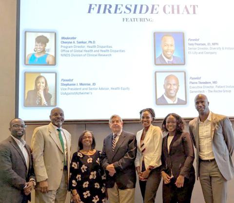Seven people stand in front of chat title slide projected on screen