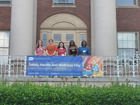 Group stands in front of Bldg. 1 behind Safety, Health and Wellness banner.