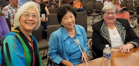 Three women scientists seated together in auditorium, smiling