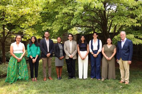 A group stands together outside, by grass, trees