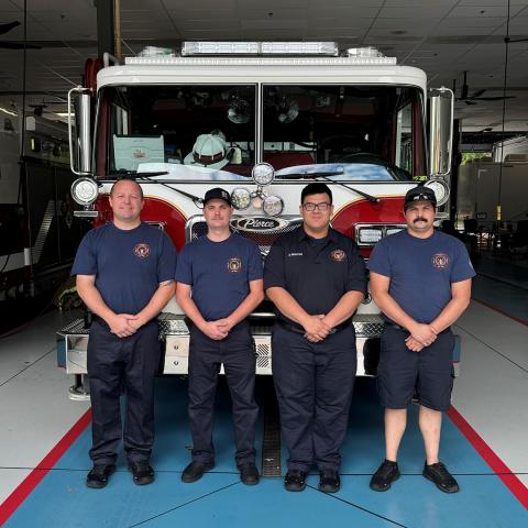 Four firefighters stand in front of a firetruck in the firehouse bay at NIH.