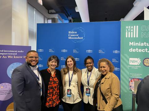 Bertagnolli poses for a photo with 4 researchers in front of a blue "Biden Cancer Moonshot" backdrop.