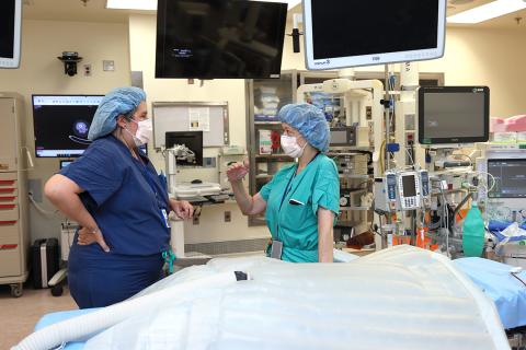 Surrounded by surgical equipment and related monitors and apparatuses, Goff and Bertagnolli, in scrubs and face masks, chat.