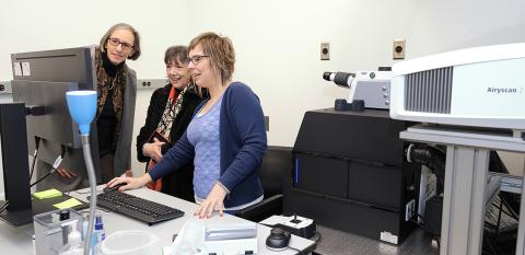 Rathmell, Bertagnolli and Ballesteros stand at desk looking with interest at computer monitor.