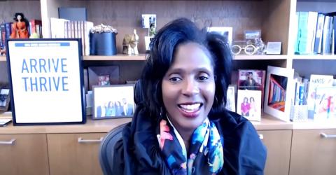 Wooten at her desk with books, photos behind her and framed saying that reads: Arrive to Thrive