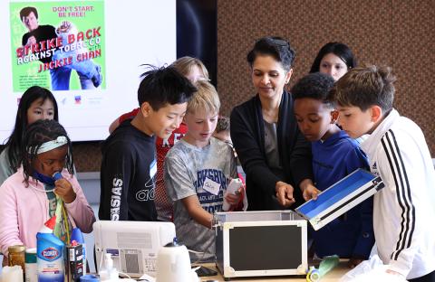 Kids look inside box at model of airways as child at left blows into tube and looks at a graph of her breathing.